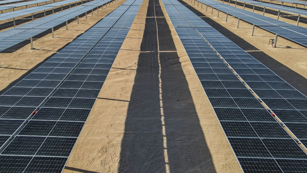 Rows of solar panels stretching into the distance on desert sand