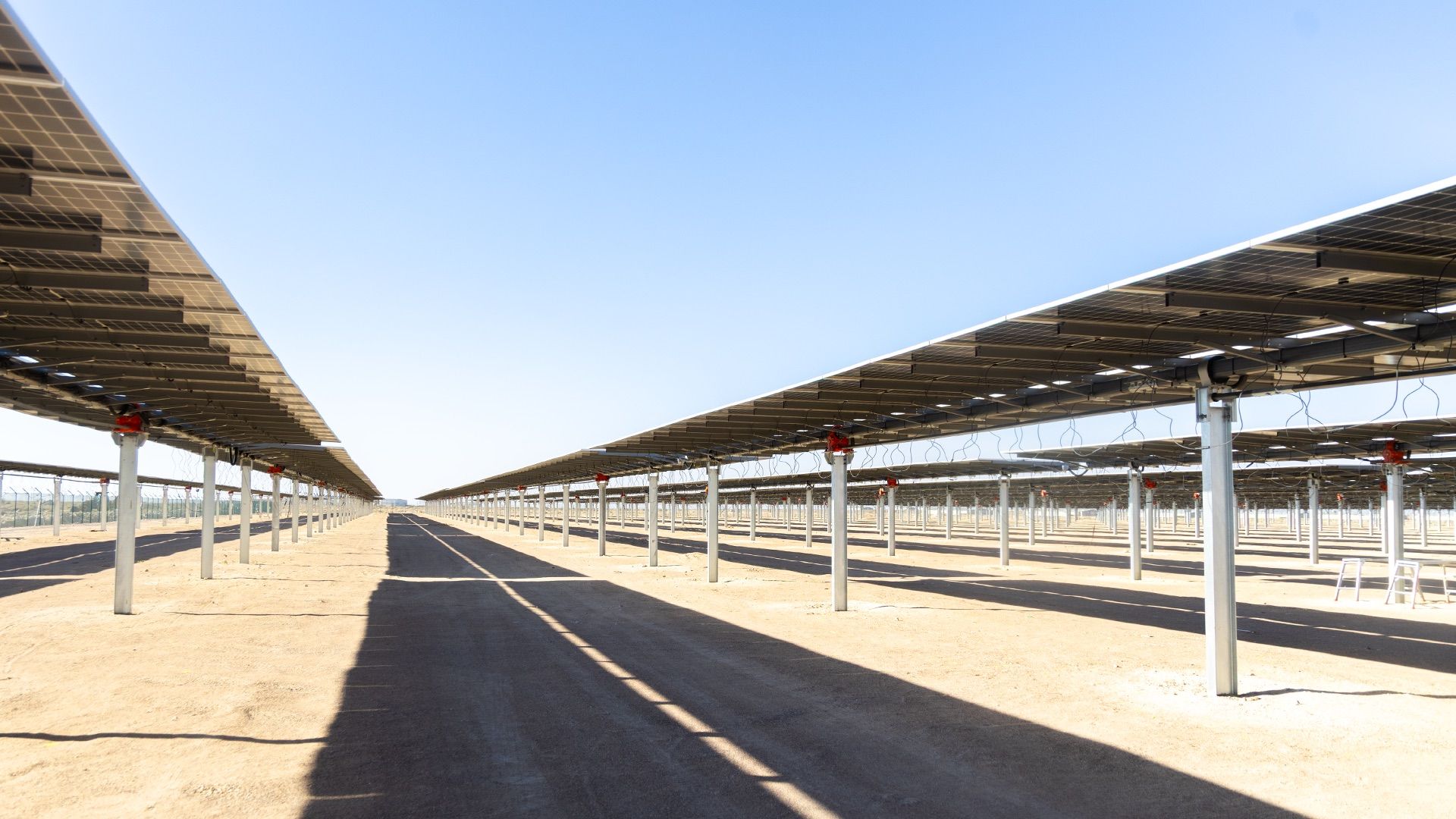Rows of single-axis solar trackers stretching to the horizon under a clear sky