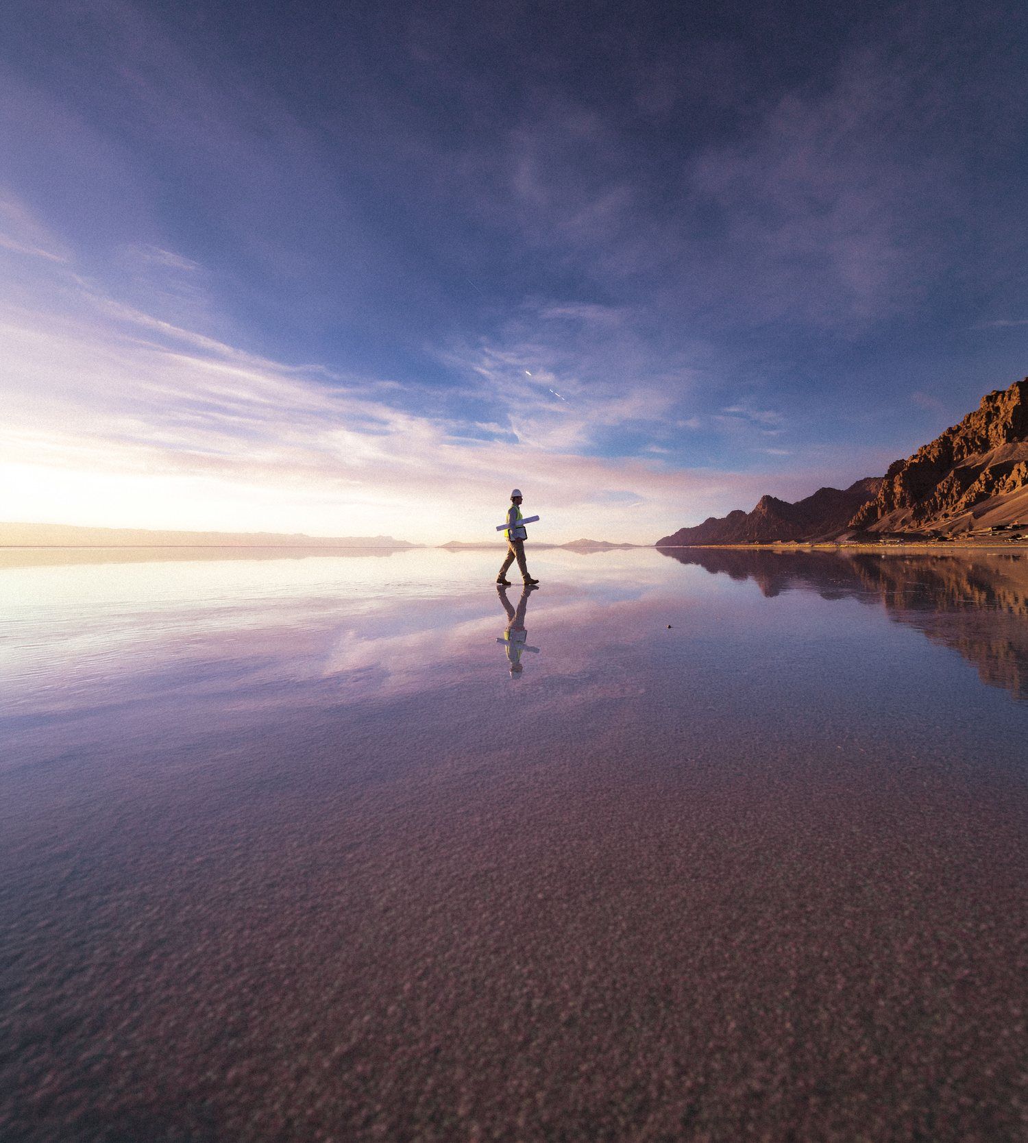 Engineer walking across a reflective salt flat at sunset, mountains on the horizon
