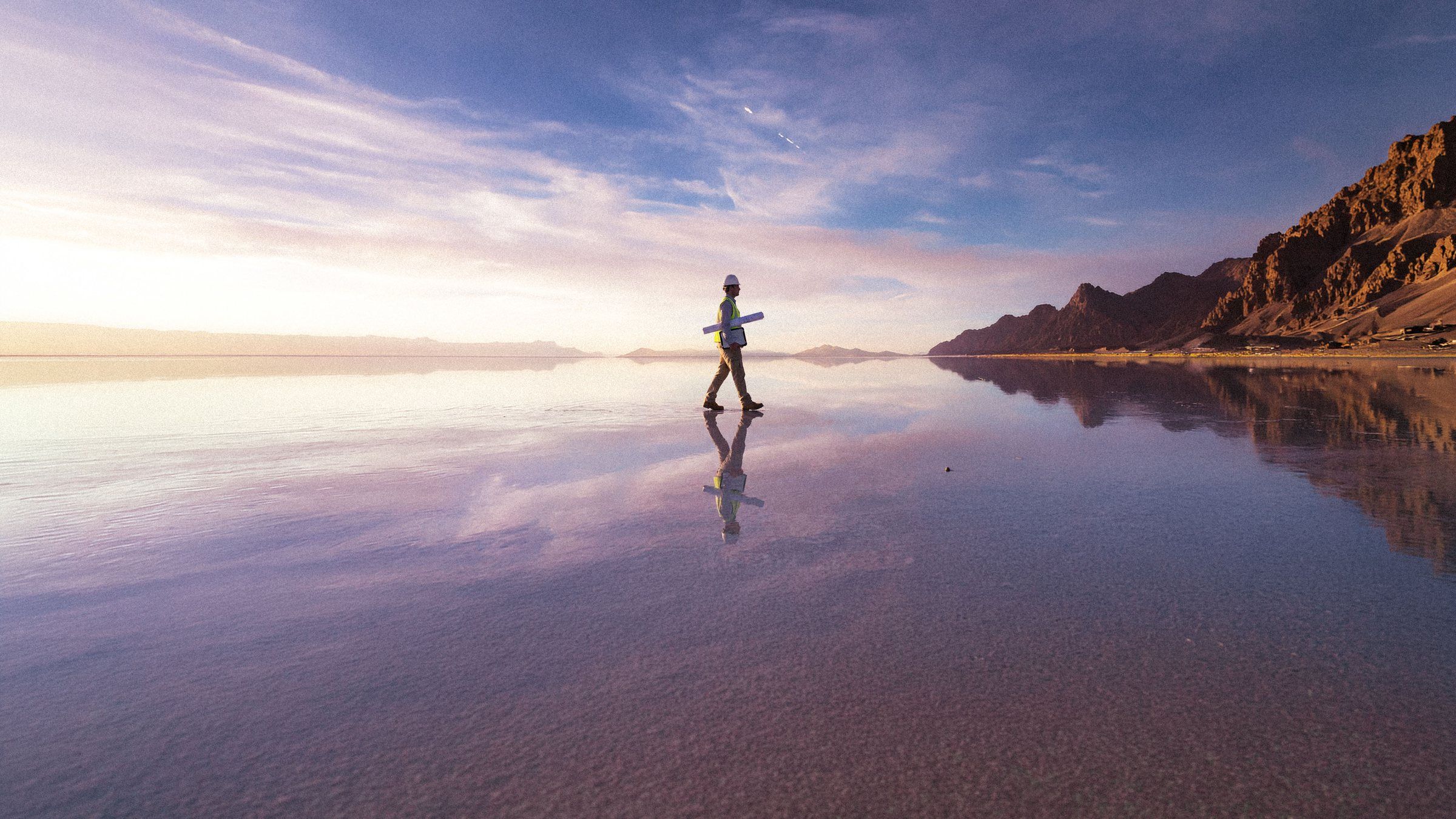 Engineer carrying drawings walks across a mirror-calm salt flat towards distant mountains